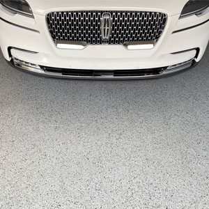 White sedan on a gray full-flake epoxy and polyaspartic-coated garage floor.